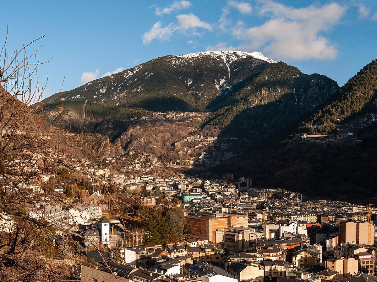 Elevated view over the dense rooftops of Andorra la Vella, with a snow-streaked Pyrenean peak rising behind the capital