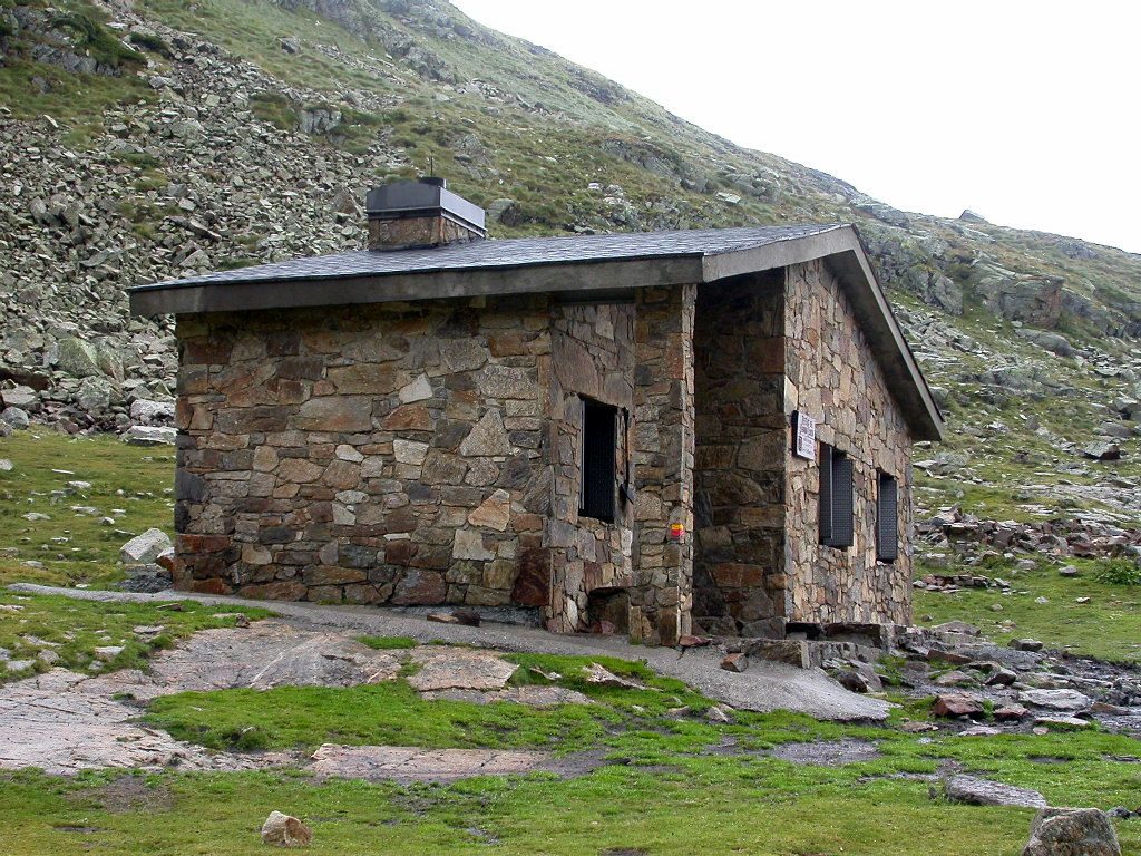 The stone Cabana Sorda mountain refuge on a grassy, boulder-strewn slope high above the Incles valley, Andorra