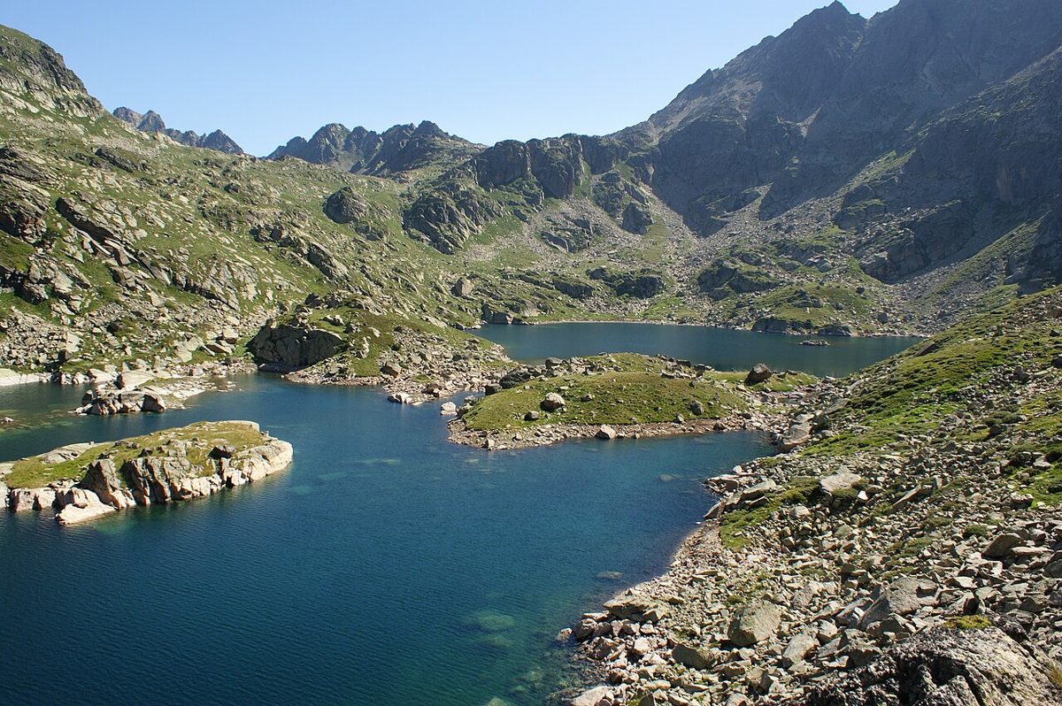 Deep blue Estany de Juclar in Andorra curving between granite outcrops and green slopes below a jagged Pyrenean ridge