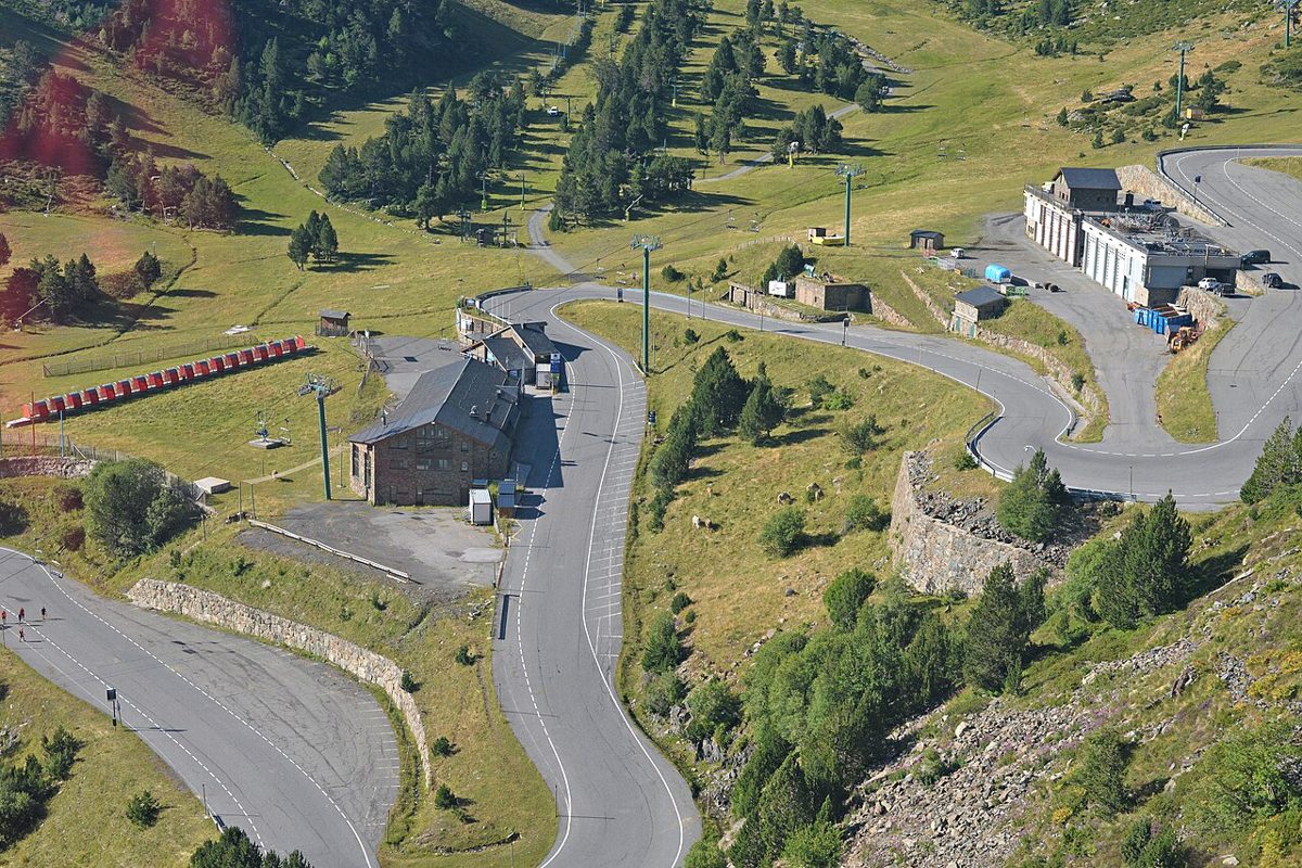 Snow-free summer view of the Ordino-Arcalis base area in Andorra, with a hairpin road, chairlifts and green alpine pasture