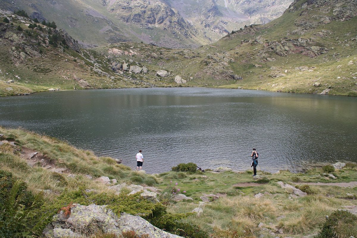 Hikers on the shore of Estany de Tristaina de Baix, the lowest Tristaina lake, in its green cirque in Ordino, Andorra